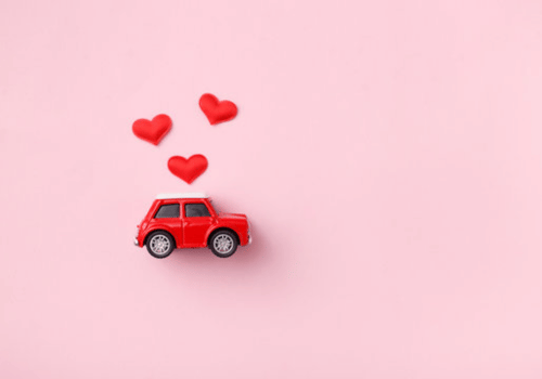 Red toy car with three red hearts on a pink background