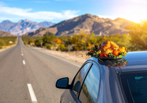 Car topped with a turkey on a tray driving on a mountain road at sunrise