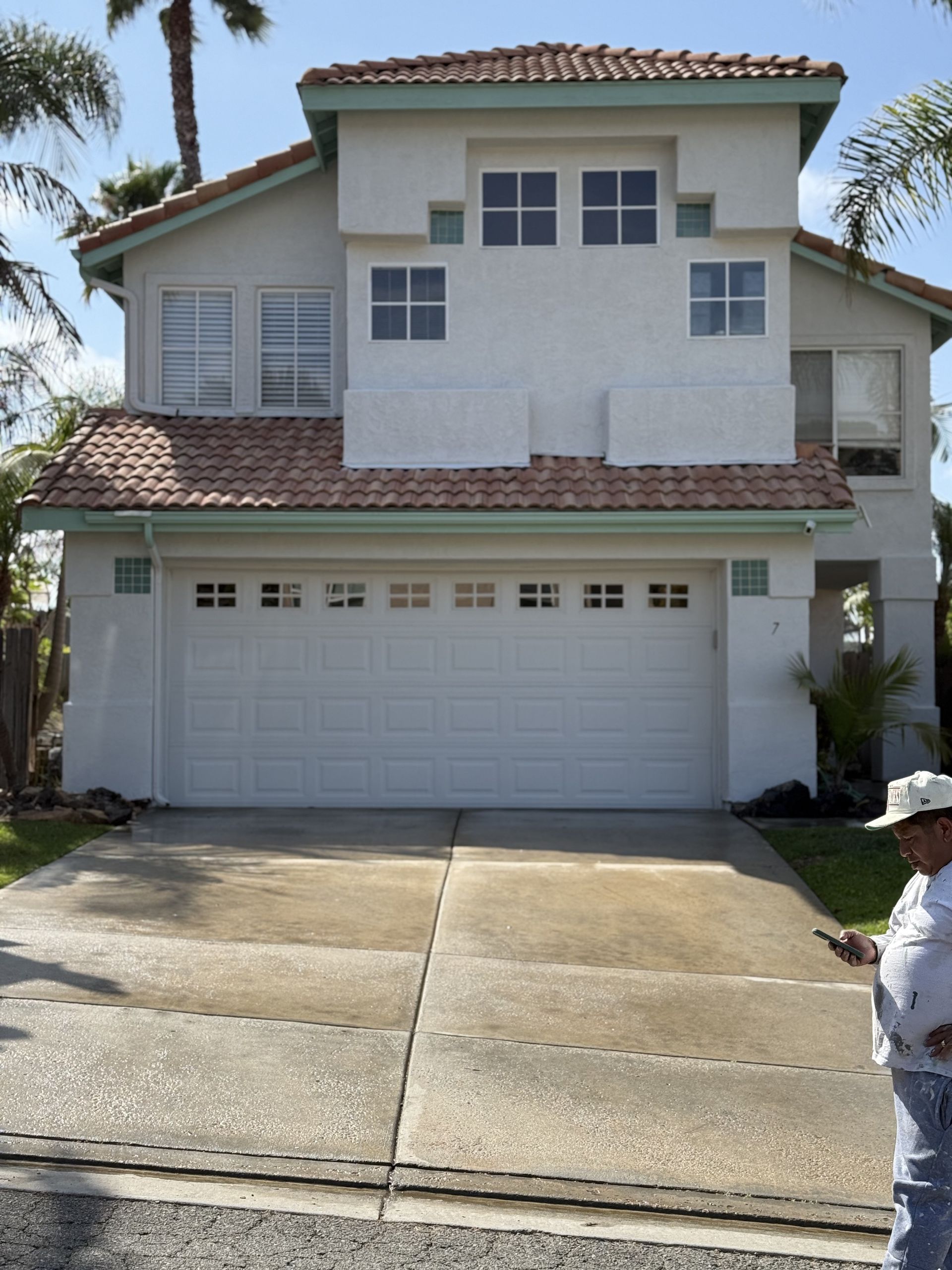 Two-story white stucco house with a double garage and driveway; a person stands at the curb.