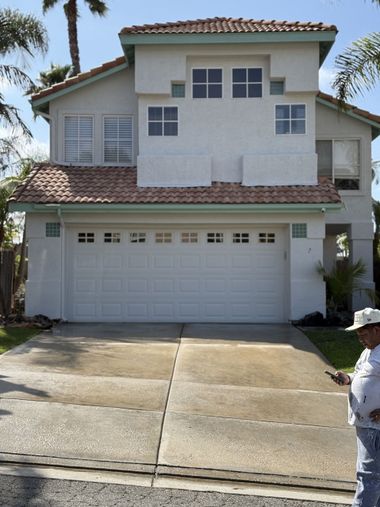 Two-story white house with a double garage and a person standing at the curb in front.