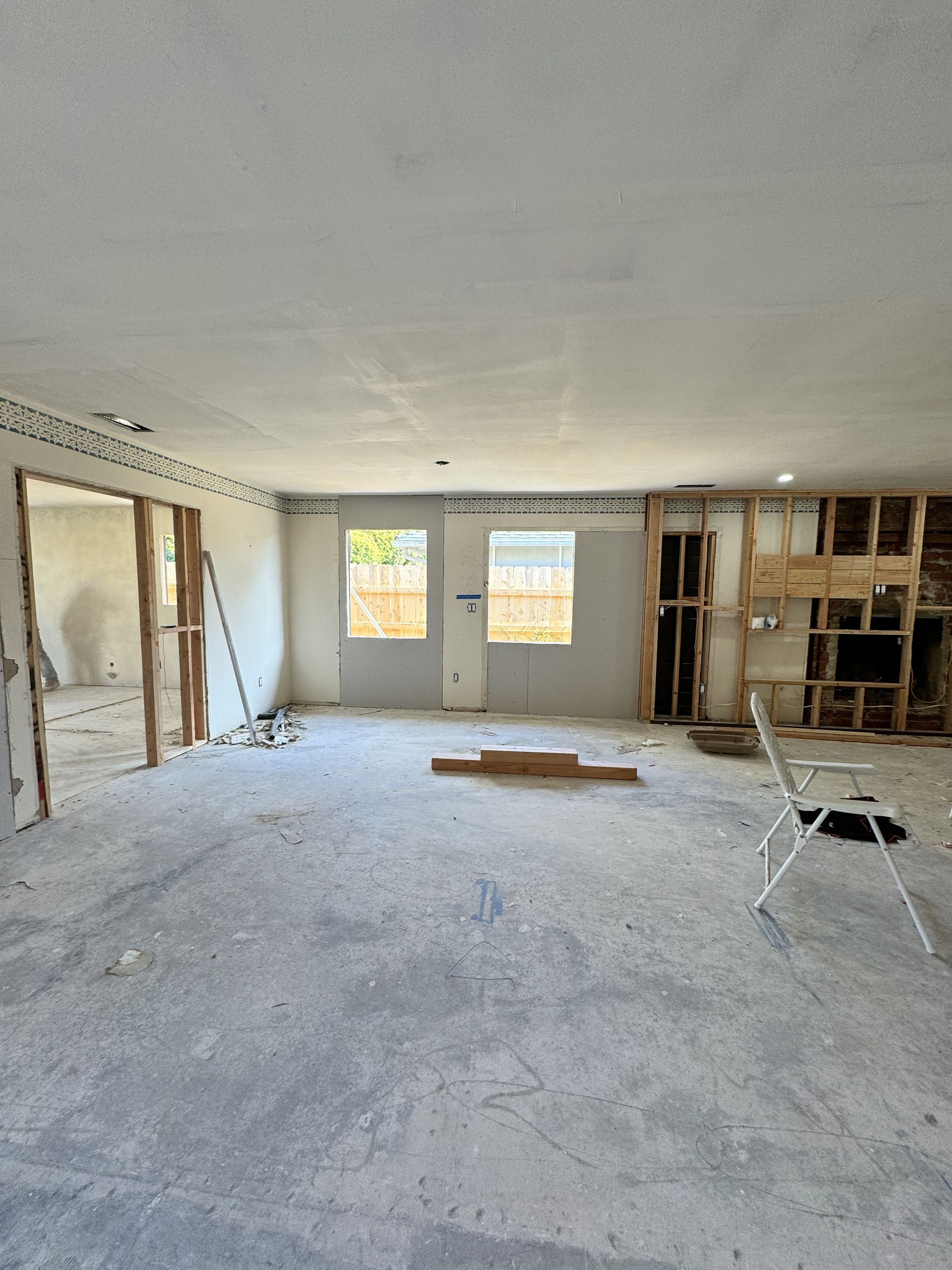 Empty room under renovation with exposed studs, unfinished walls, debris, and two windows at the back.