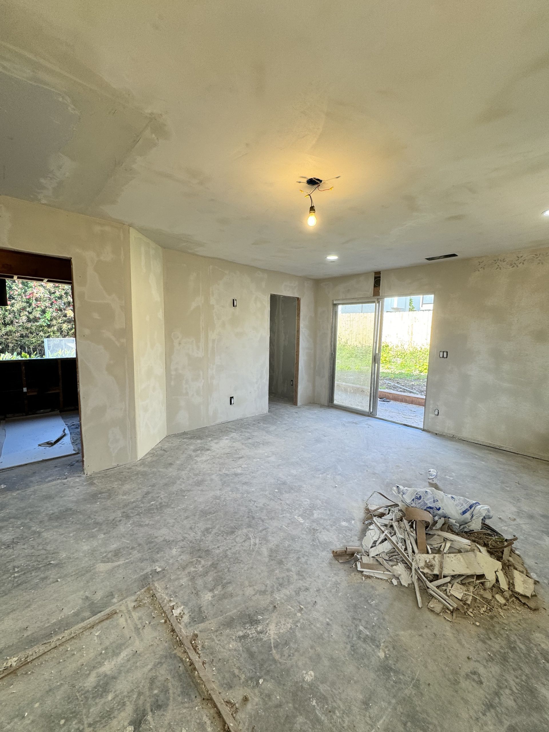 Empty renovated room with unfinished walls, bare concrete floor, and debris pile near the center.