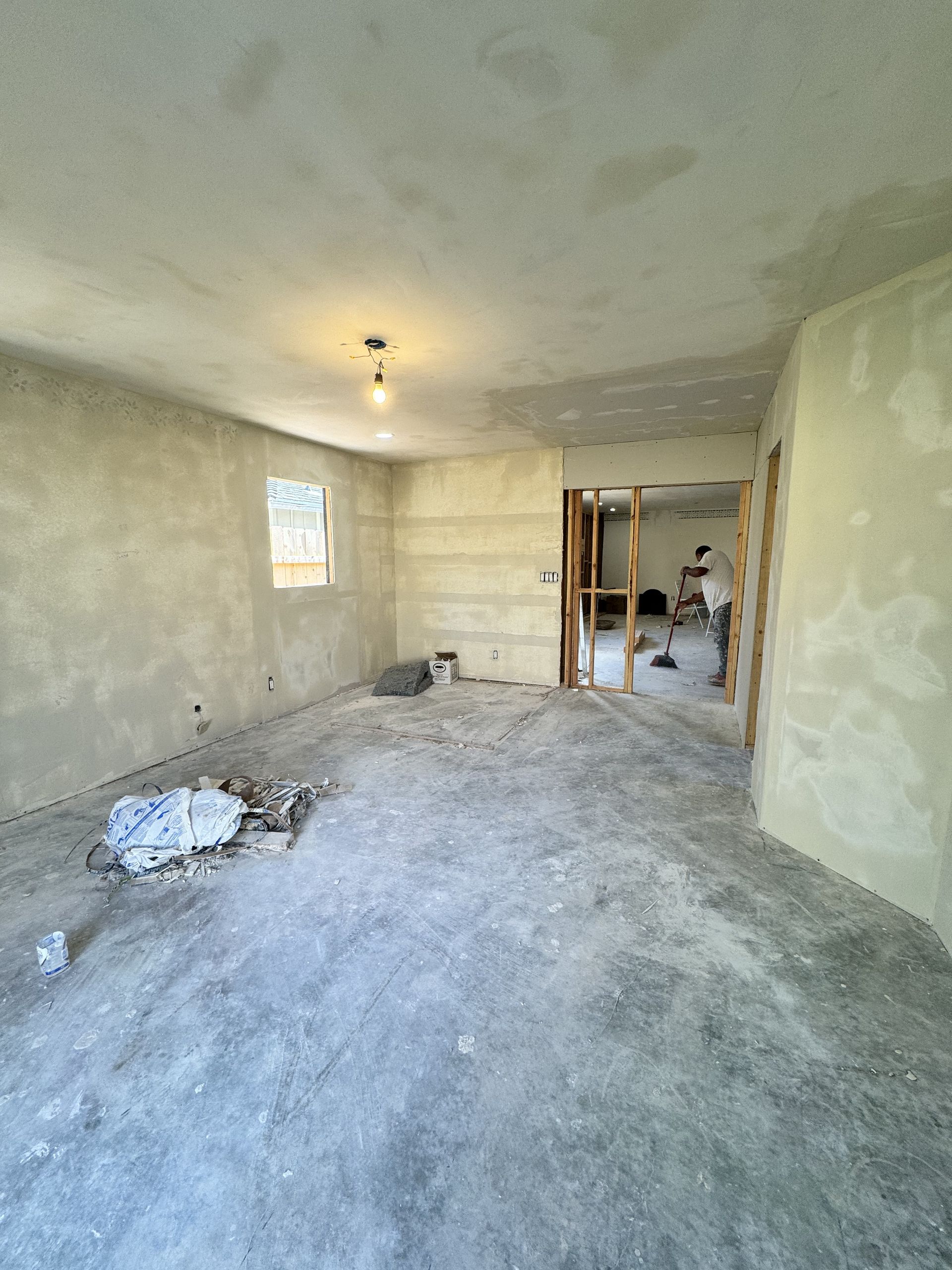 Renovated empty room with unfinished walls, debris on floor, and a doorway to another space