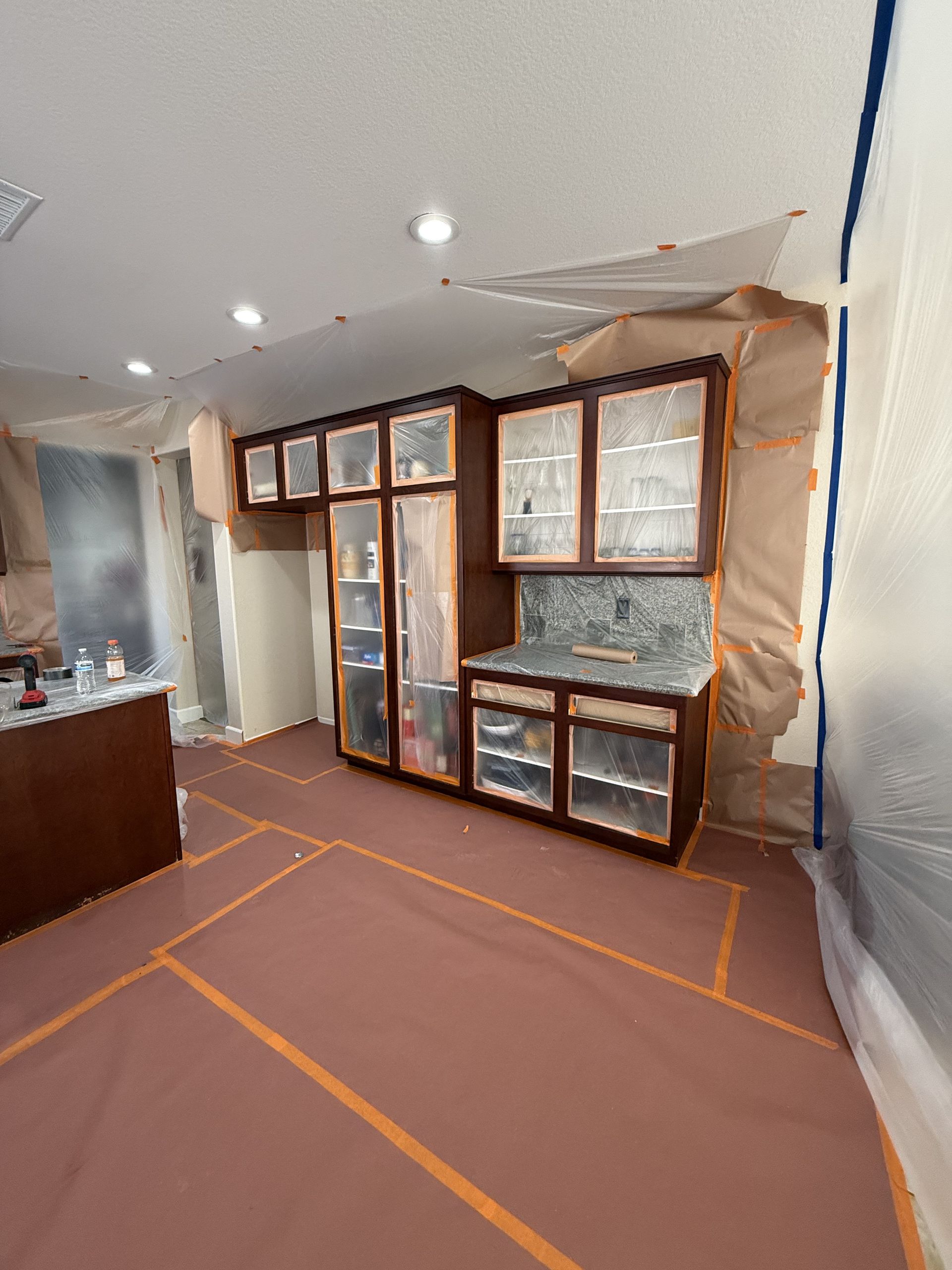 Living room under renovation with taped floor, plastic-covered walls, and newly installed windows and cabinets