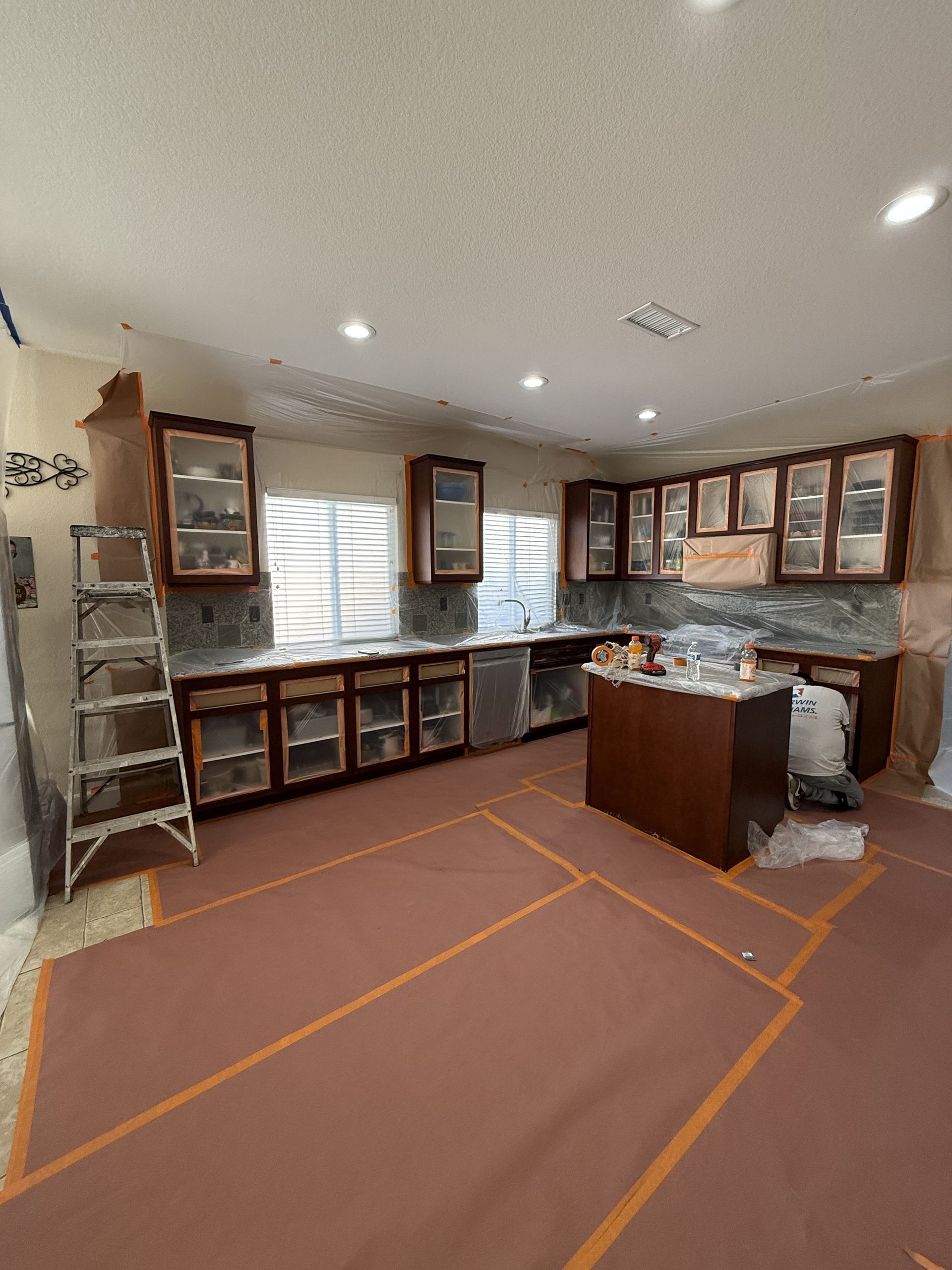 Unfinished kitchen with cabinets, ladder, and taped floor layout under bright recessed lights