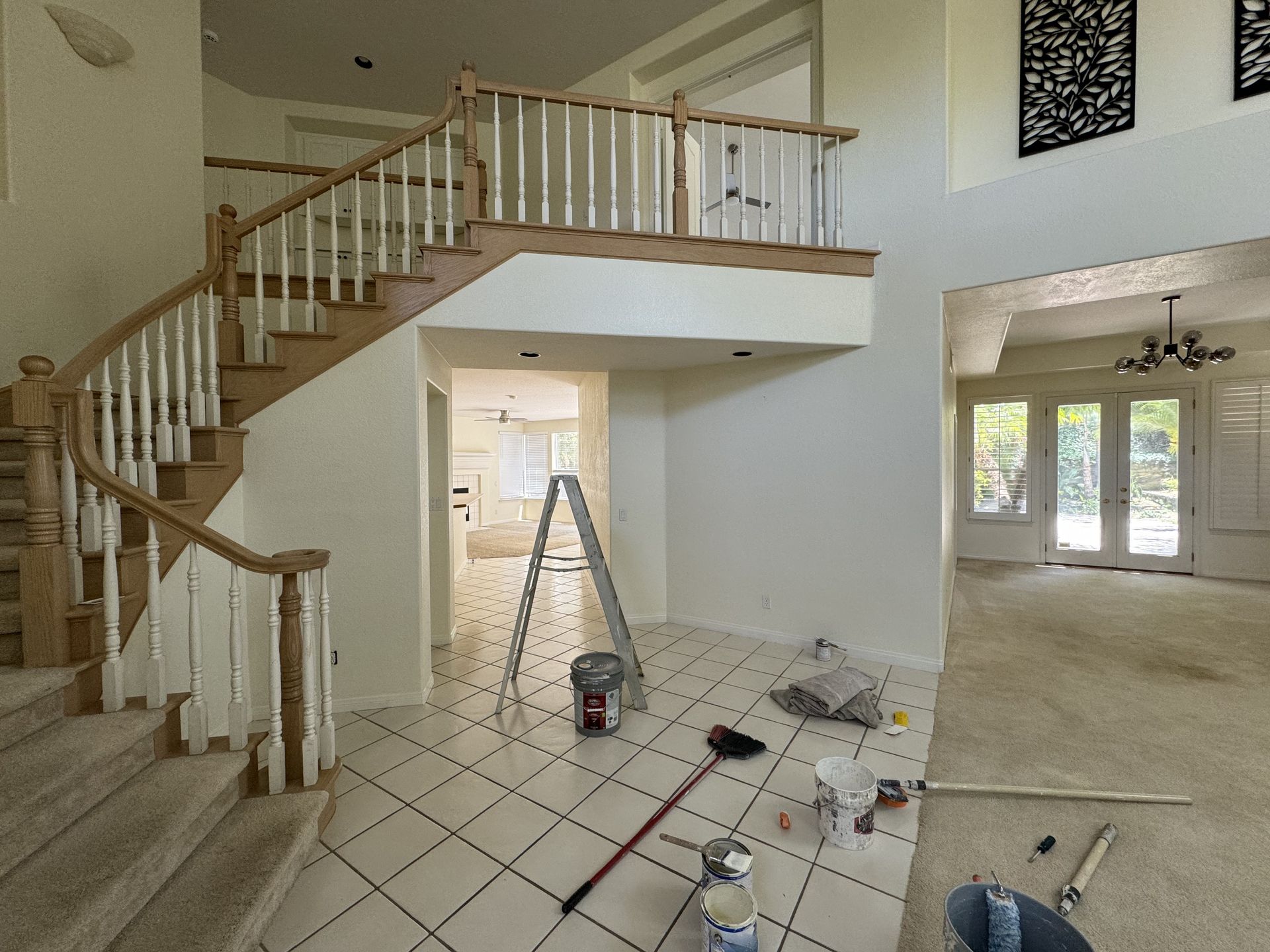 Interior under renovation with staircase, tiled floor, ladder, and scattered tools in a bright foyer