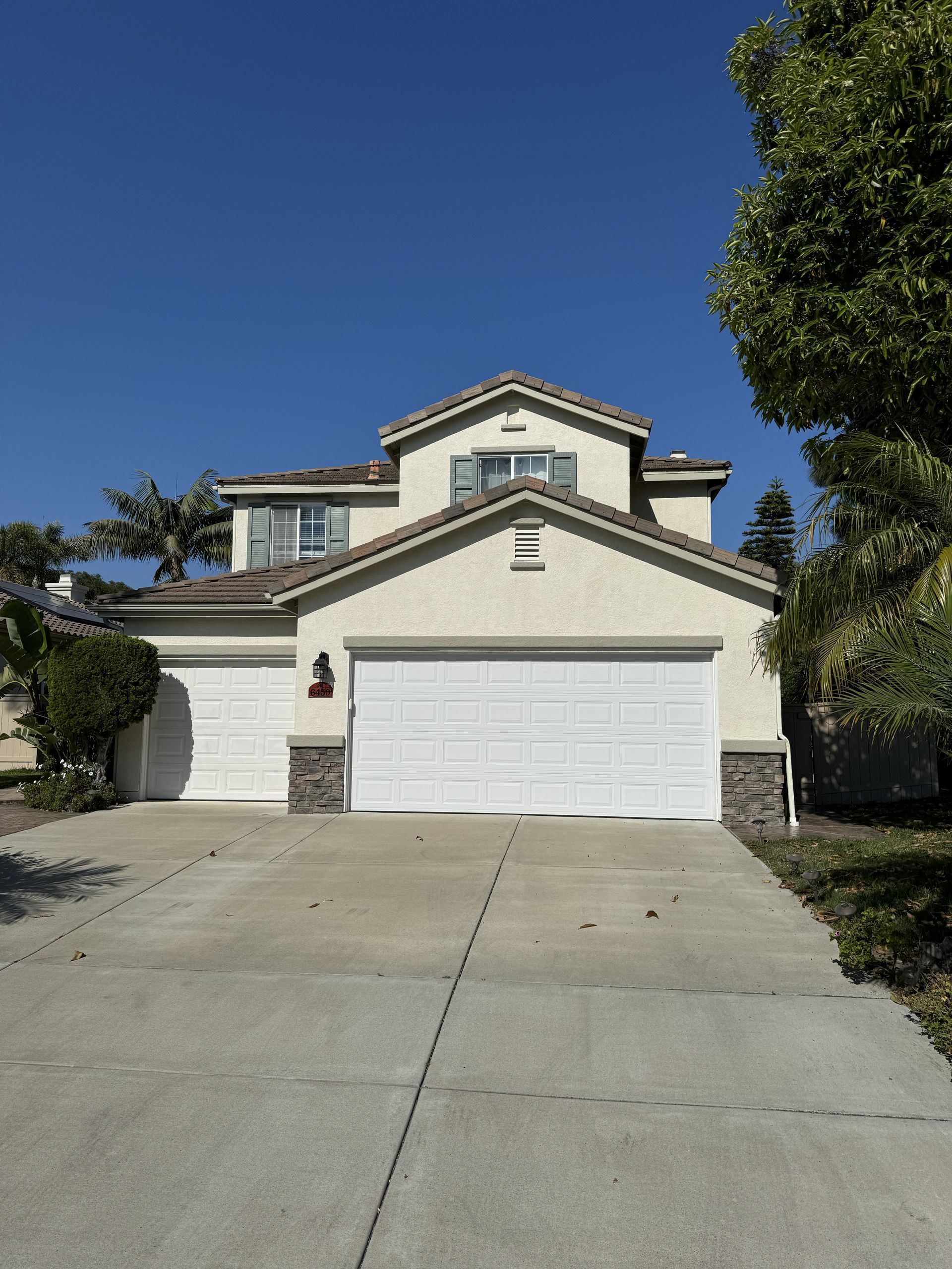 Suburban two-story house with a white garage, concrete driveway, and blue sky.