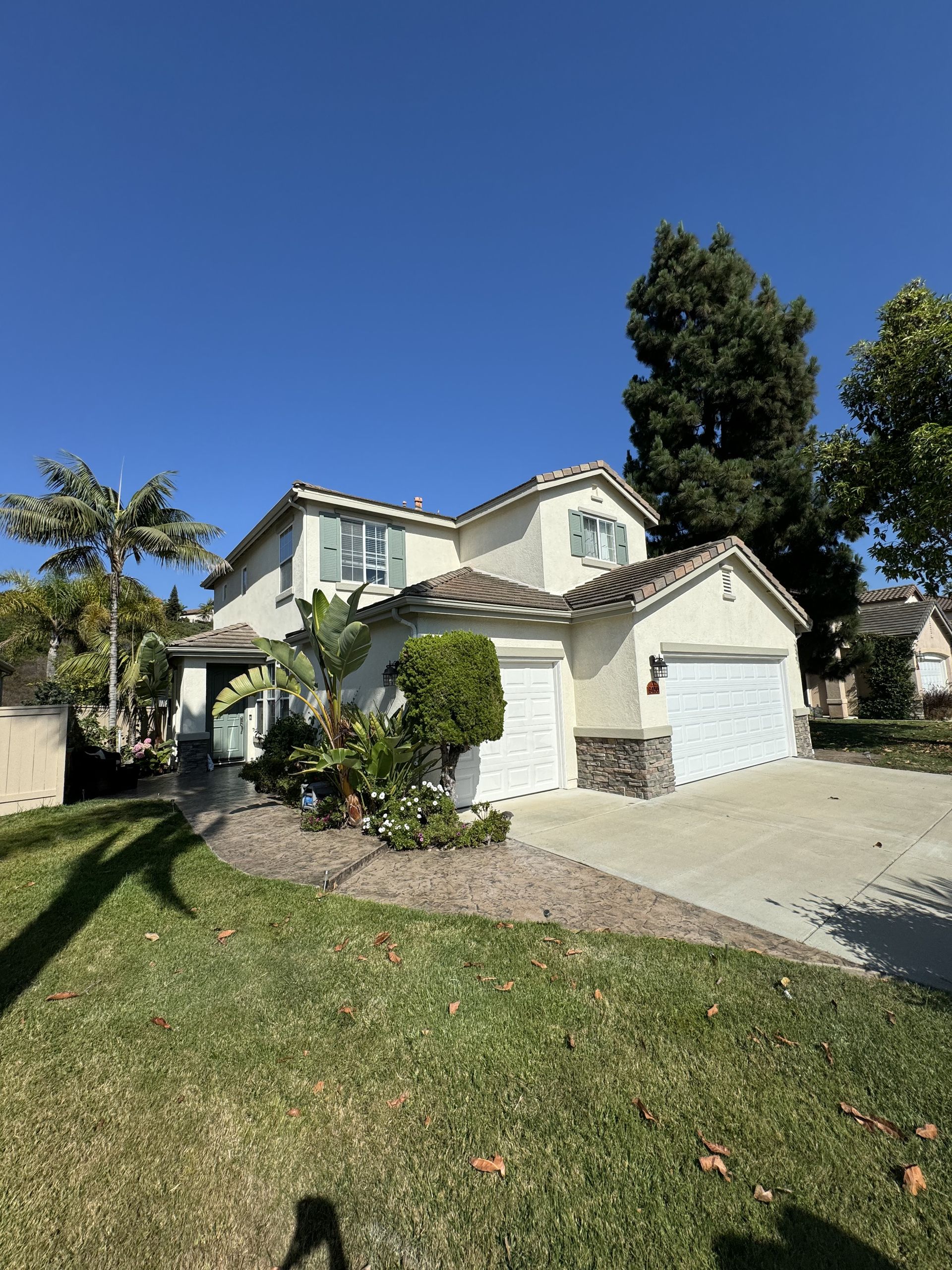 Suburban two-story house with white garage, driveway, and green lawn under a clear blue sky