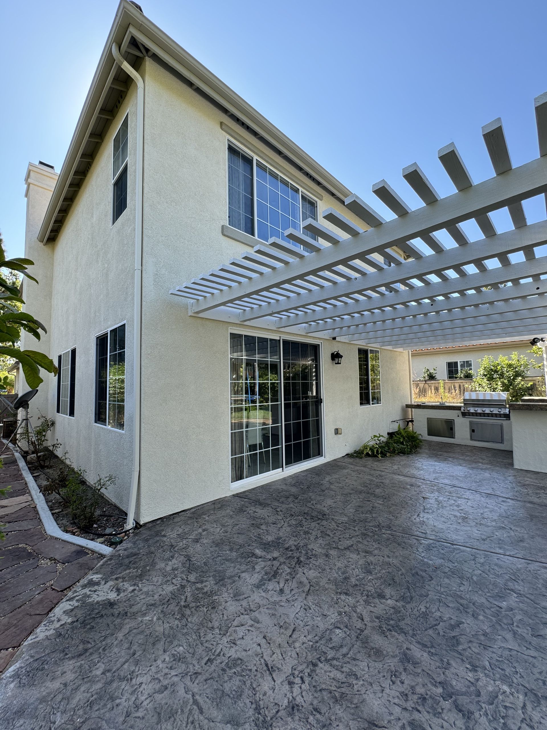 Two-story white stucco house with pergola-covered driveway and landscaped front yard