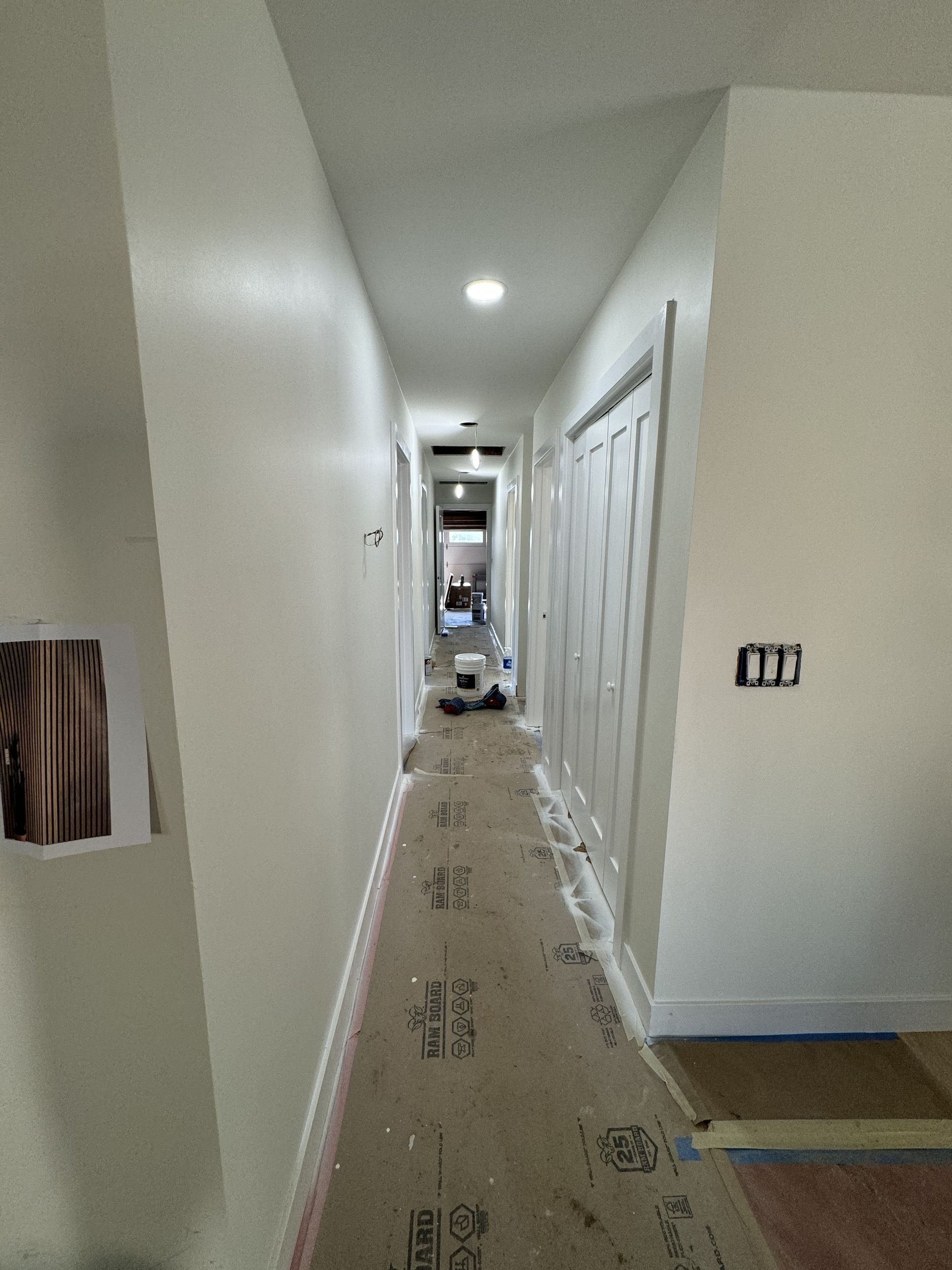Narrow white hallway with doors on both sides and a protective floor covering during renovation.