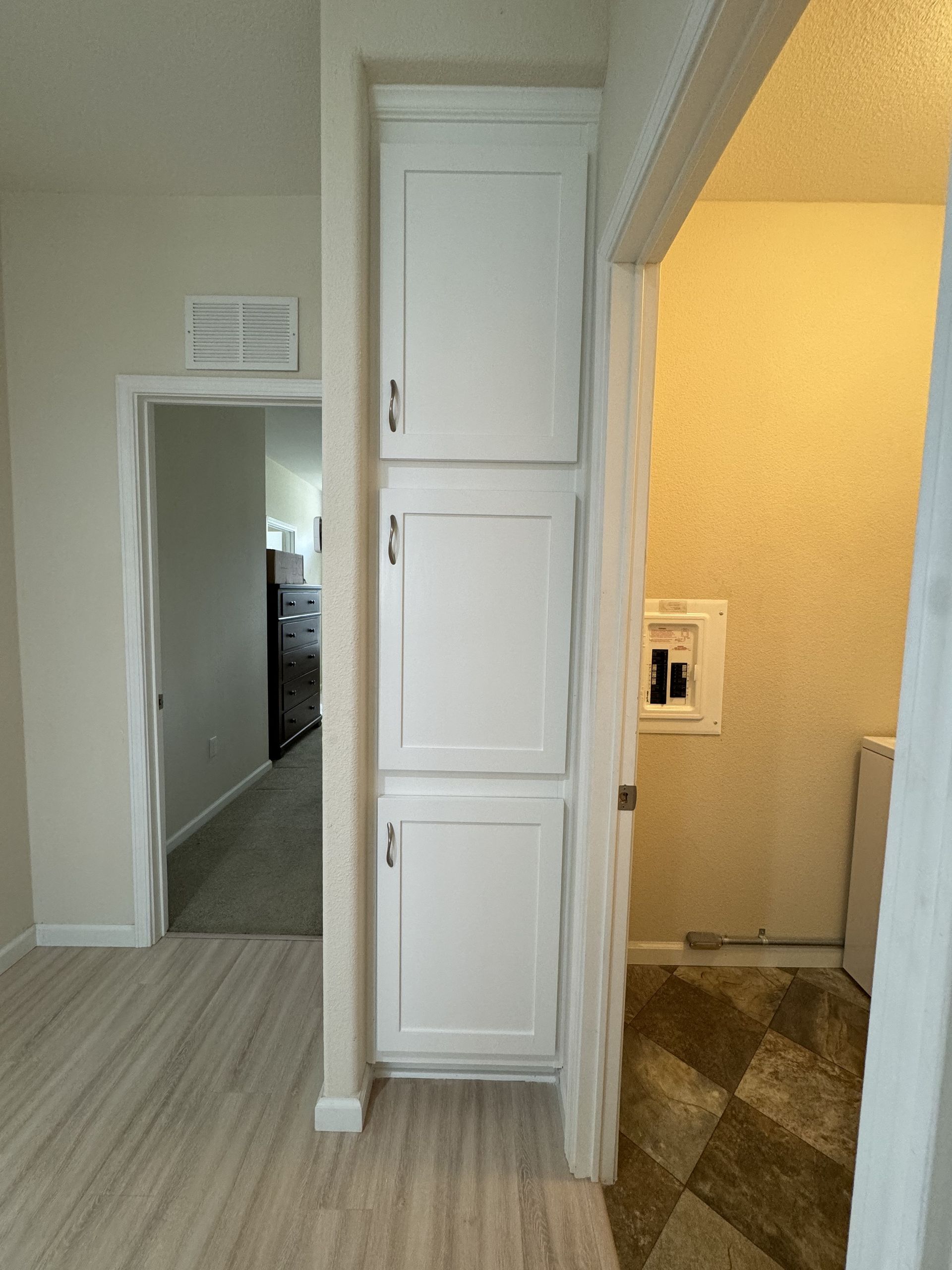 Hallway with white built-in cabinets, doorway to carpeted room, and tiled area near a lit bathroom.