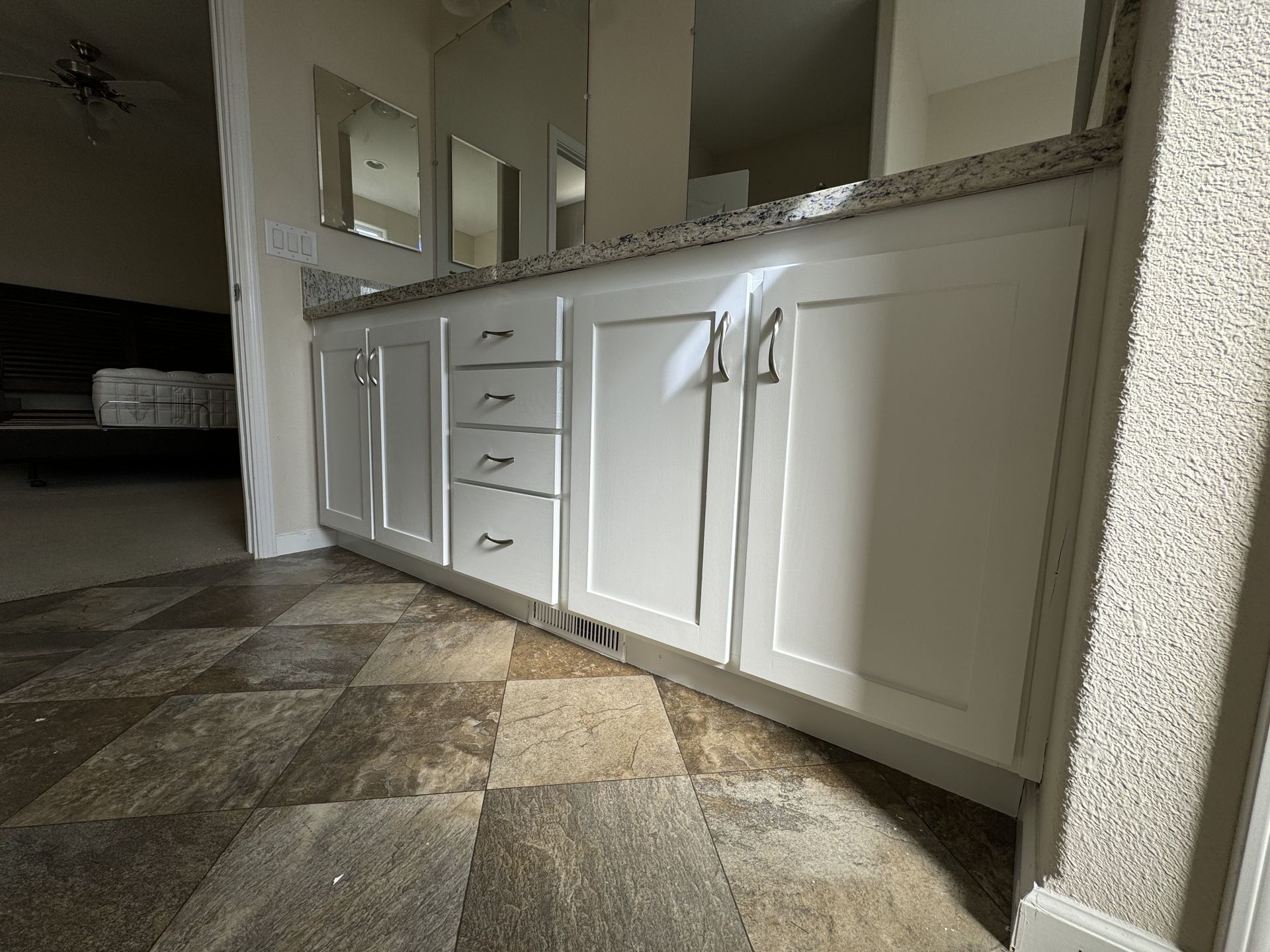White bathroom vanity with drawers and cabinets beside a sink in a tiled room