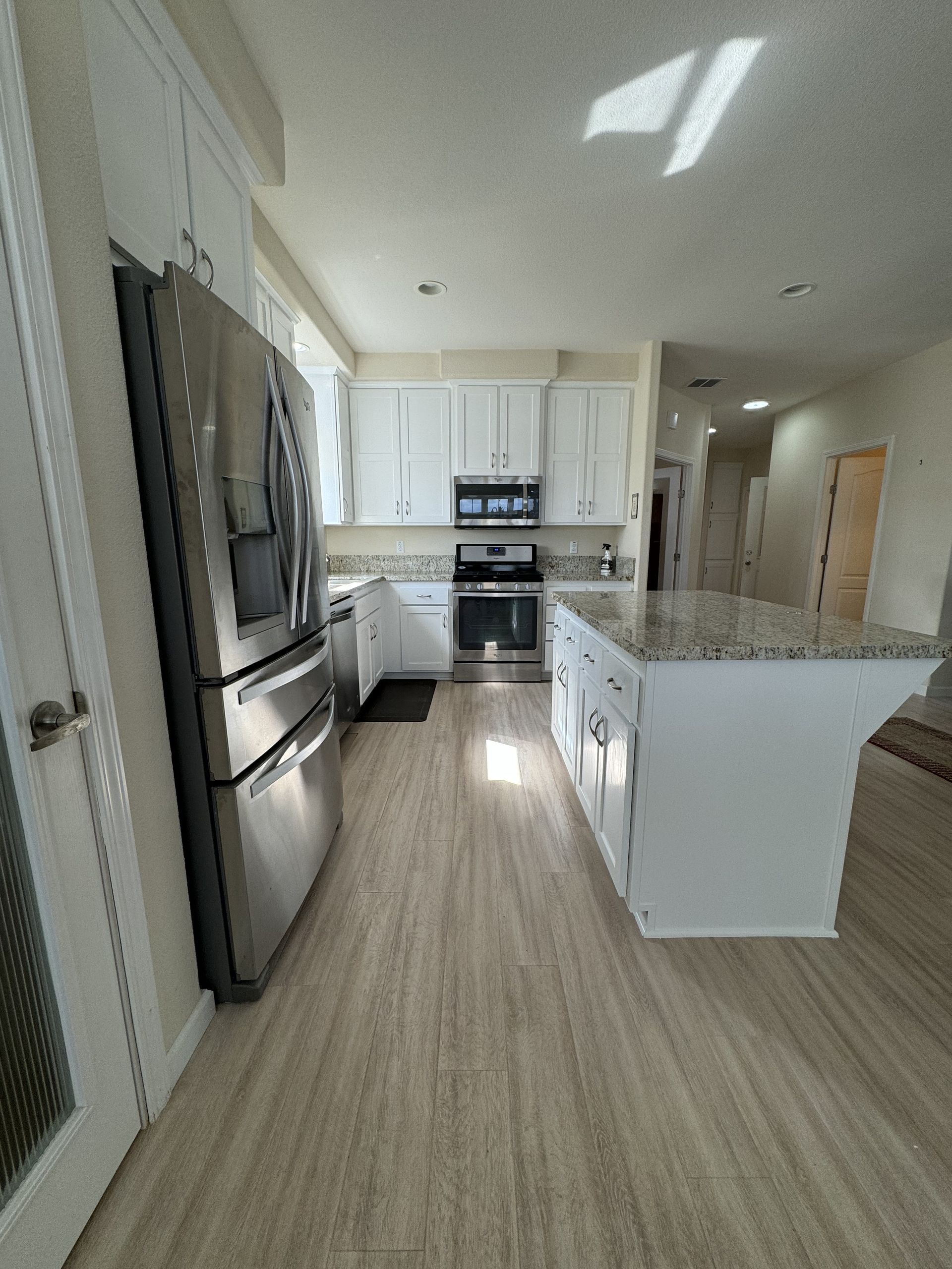 Bright modern kitchen with white cabinets, stainless appliances, and a large granite island