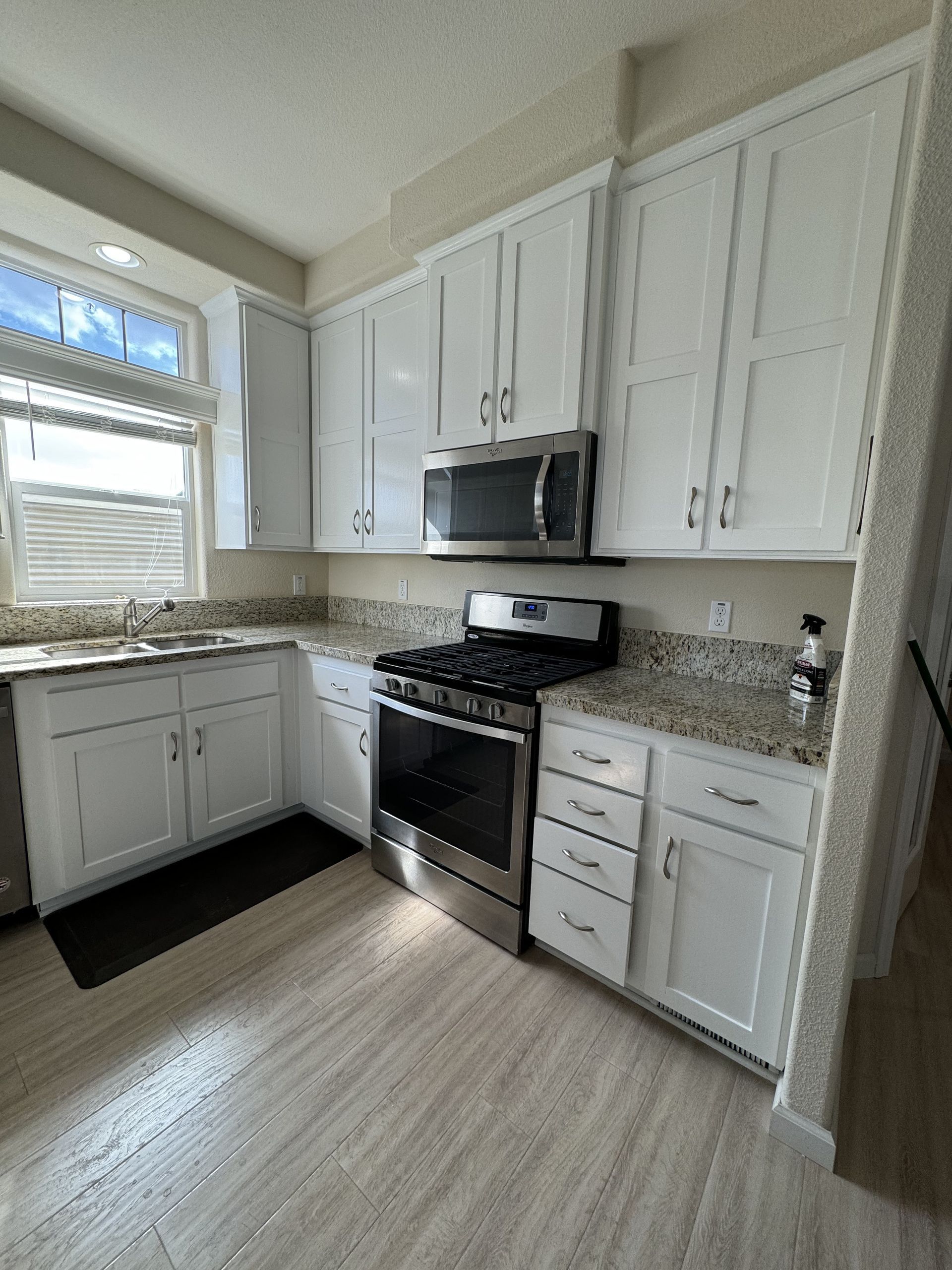 Bright white kitchen with stainless steel stove and microwave, granite counters, and window above sink.