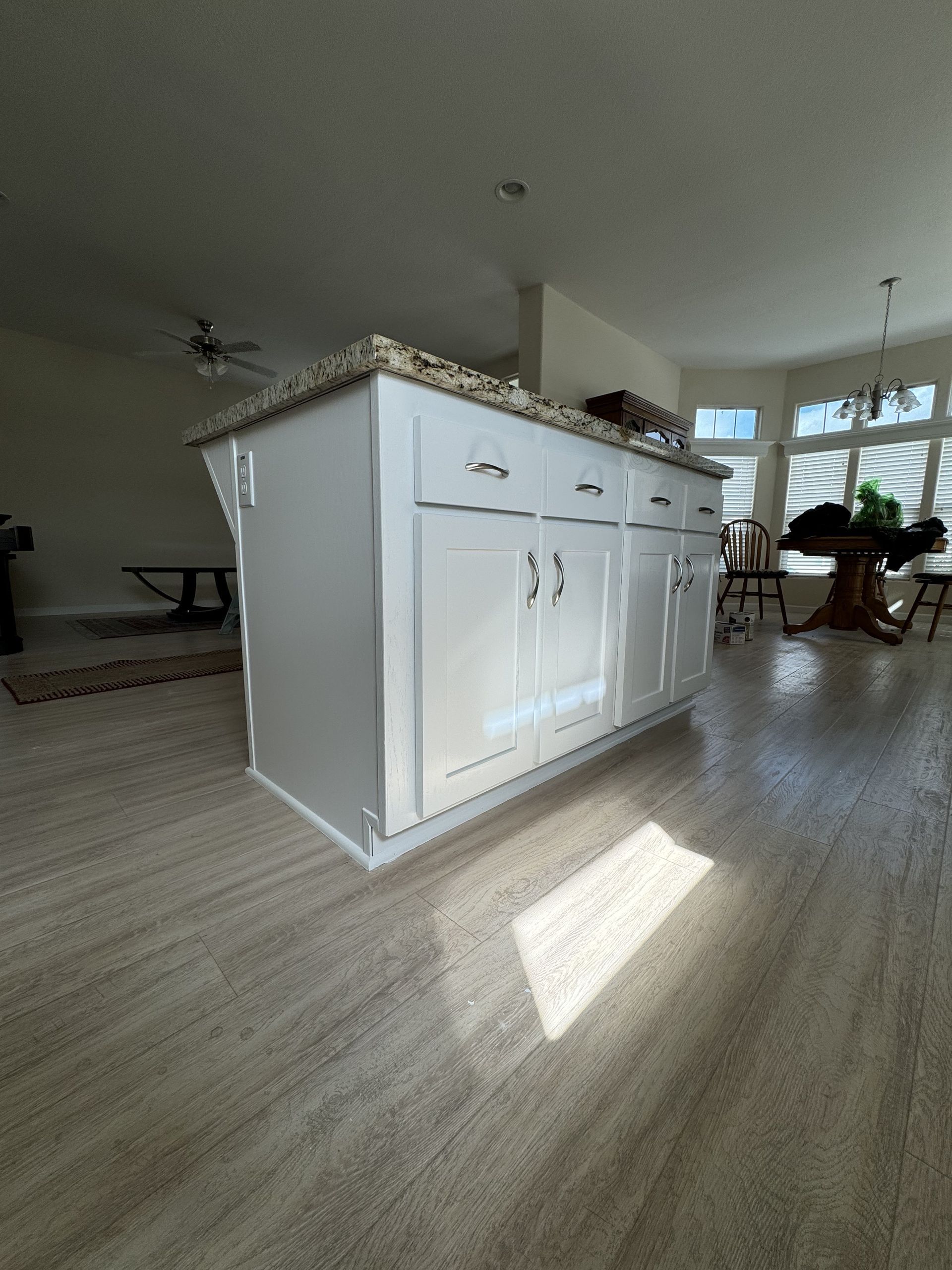 Bright kitchen with white island cabinets, wood floors, and sunlight near large windows