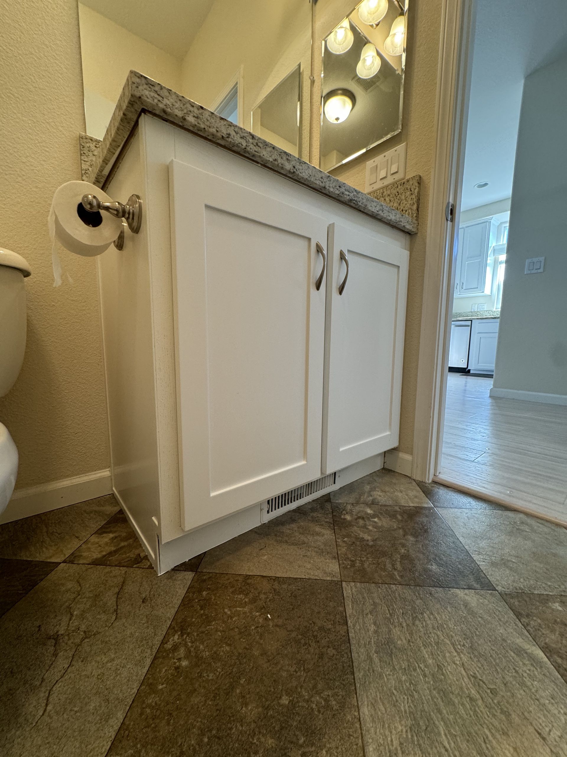 White bathroom vanity cabinet under a granite countertop with a sink and wall mirror in a tiled room