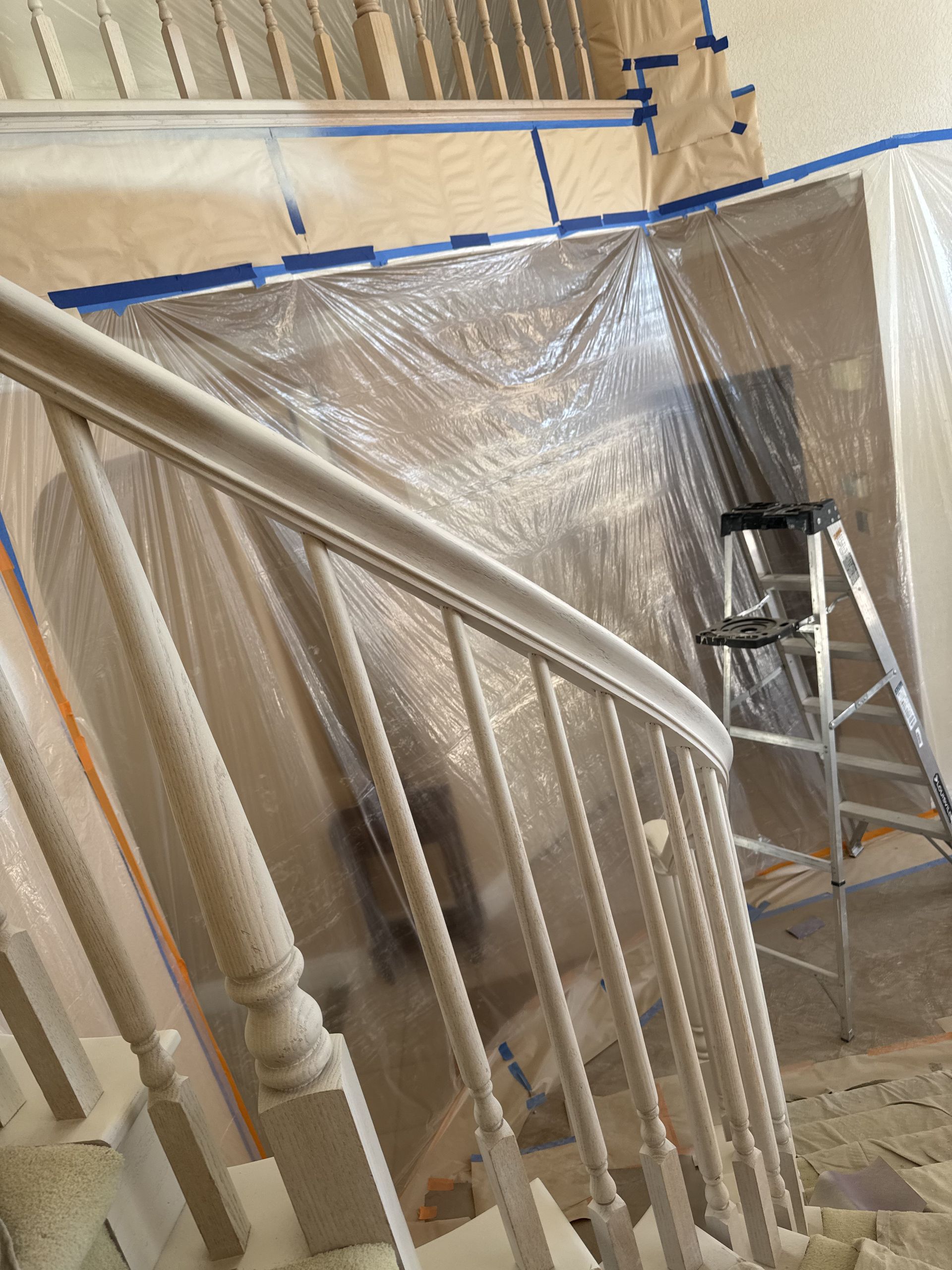 Plastic-covered stairwell under renovation, with taped rails and a metal ladder nearby.