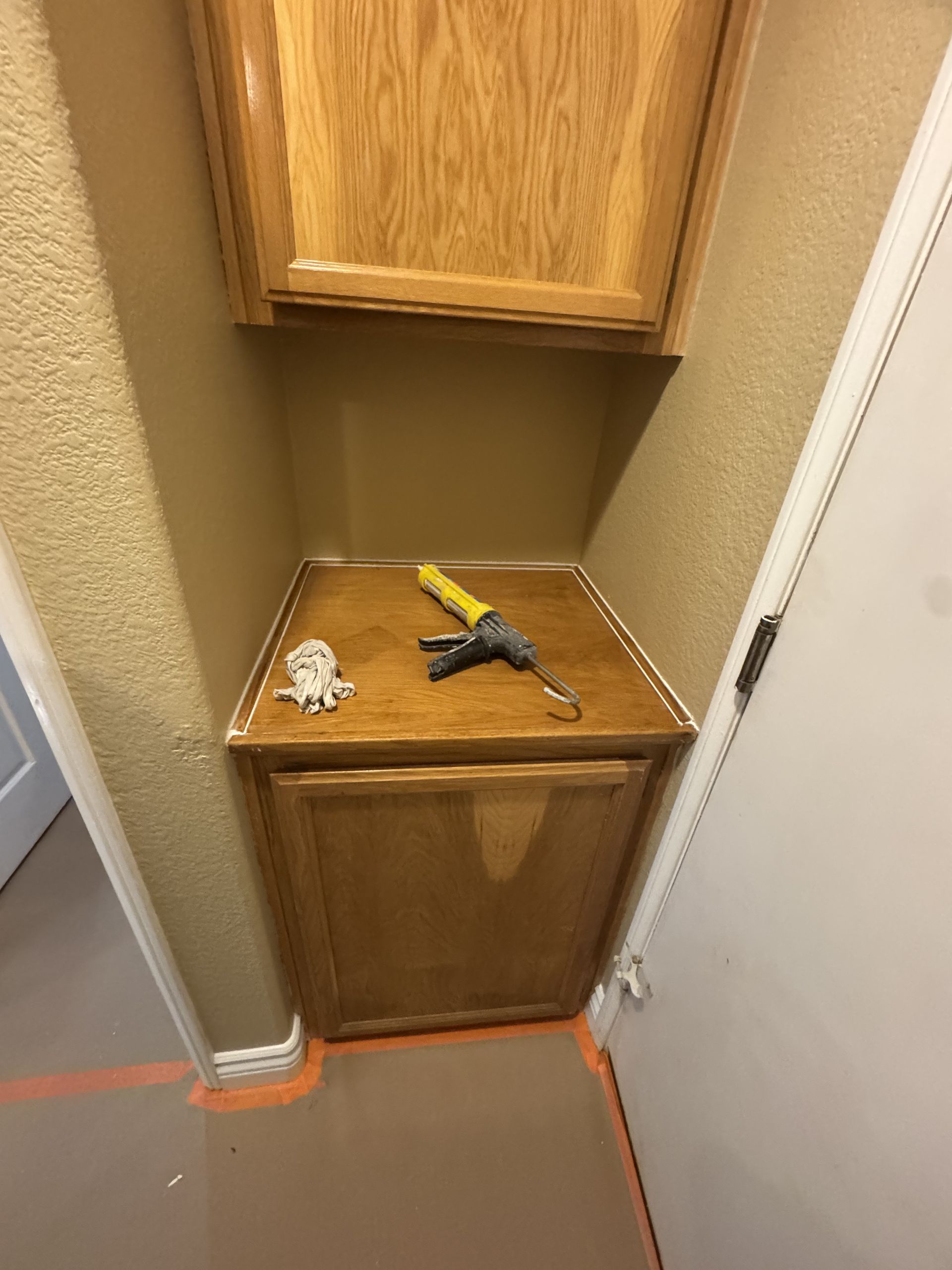 Wooden cabinet alcove with a yellow-and-black tool and a crumpled tissue on the shelf.