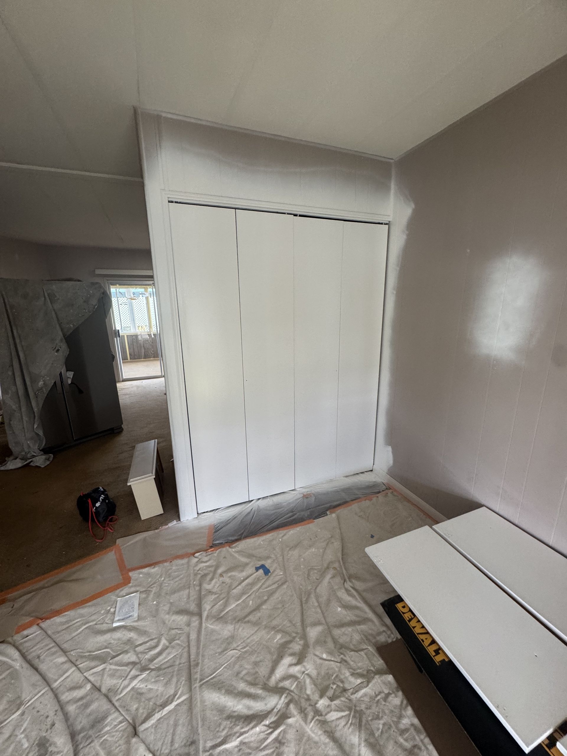 Small room with white closet doors, tarp-covered floor, and a few construction materials.
