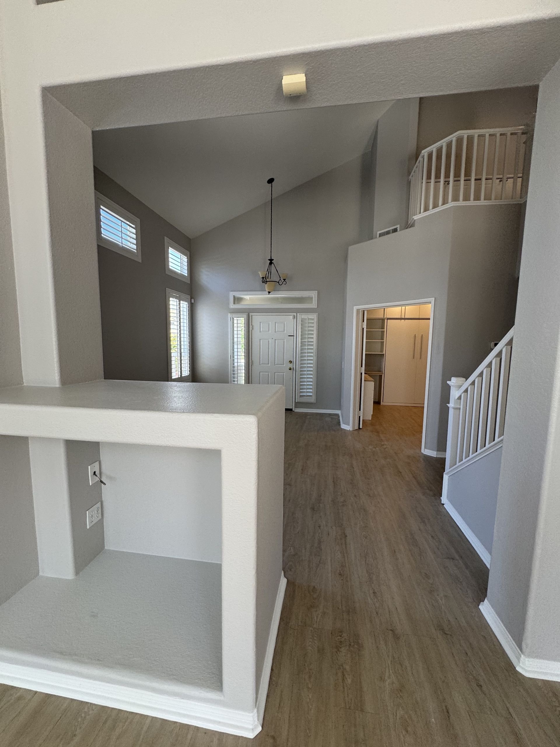 Modern home entryway with high ceiling, staircase, white walls, and a front door at the back.