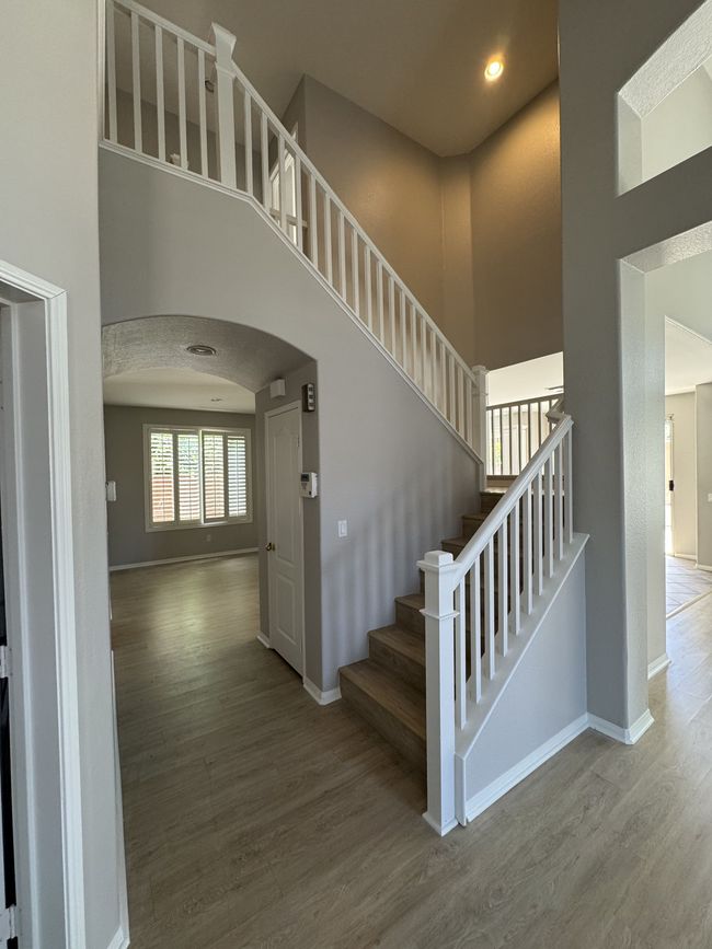 Bright foyer with gray walls, wood floors, and a staircase with white railings leading upstairs.
