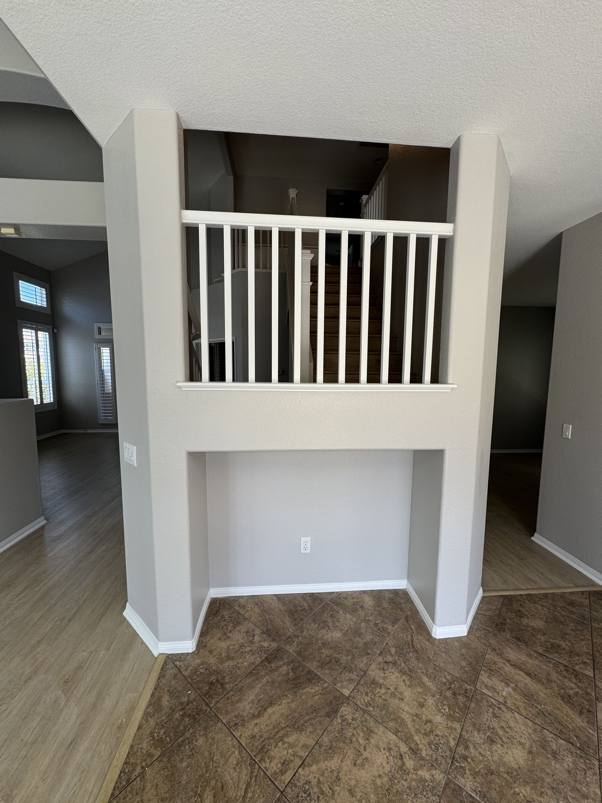 Living room nook with white railing overlook and alcove beneath, framed by beige walls and wood flooring