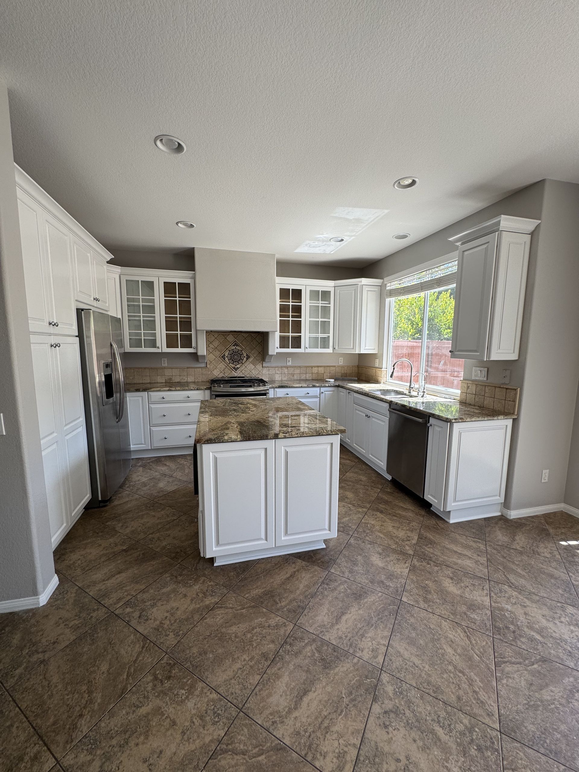 Bright modern kitchen with white cabinets, granite counters, island, and tiled floor