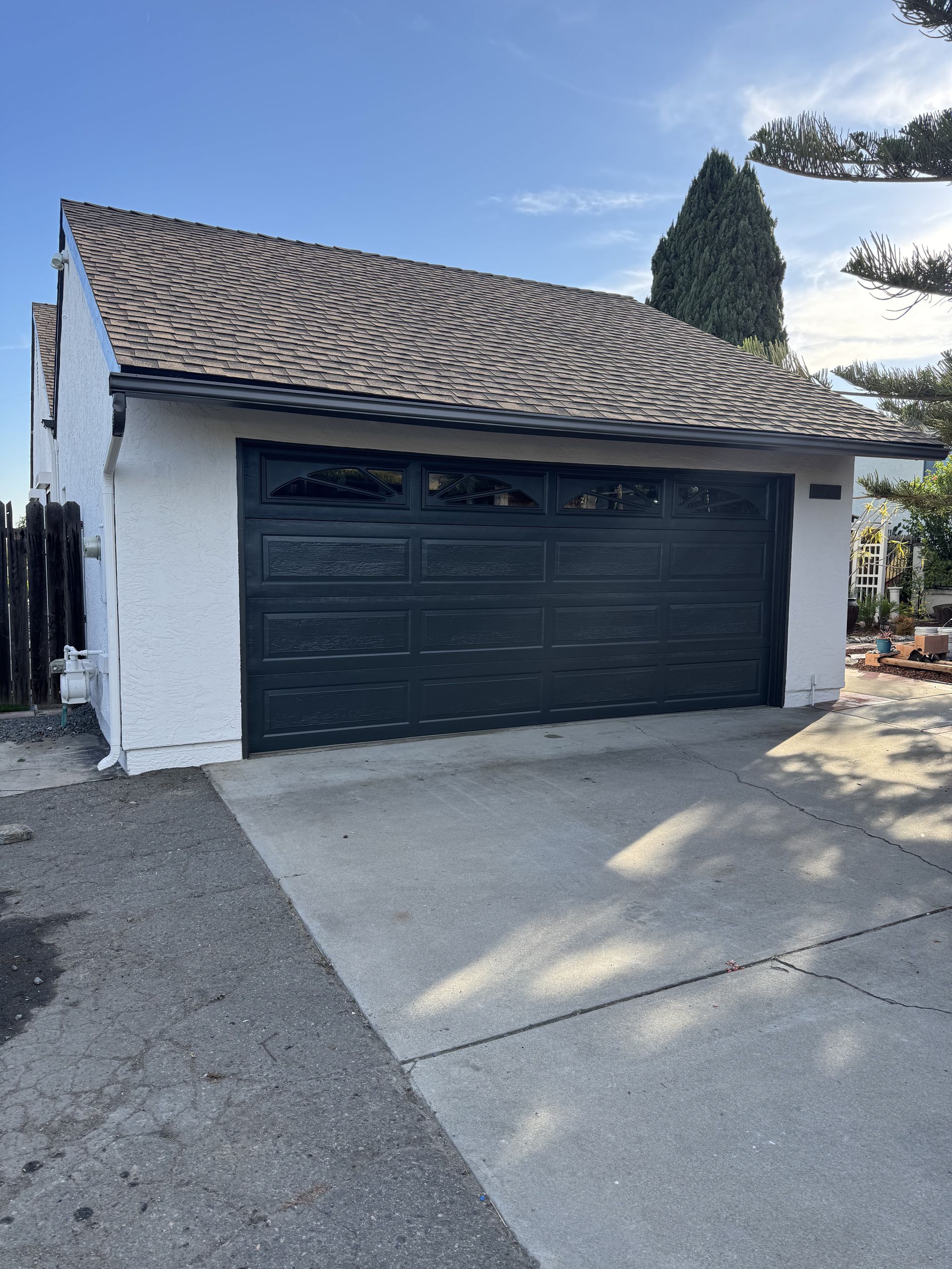 White house with black garage door and a sloped tile roof, viewed from a driveway.