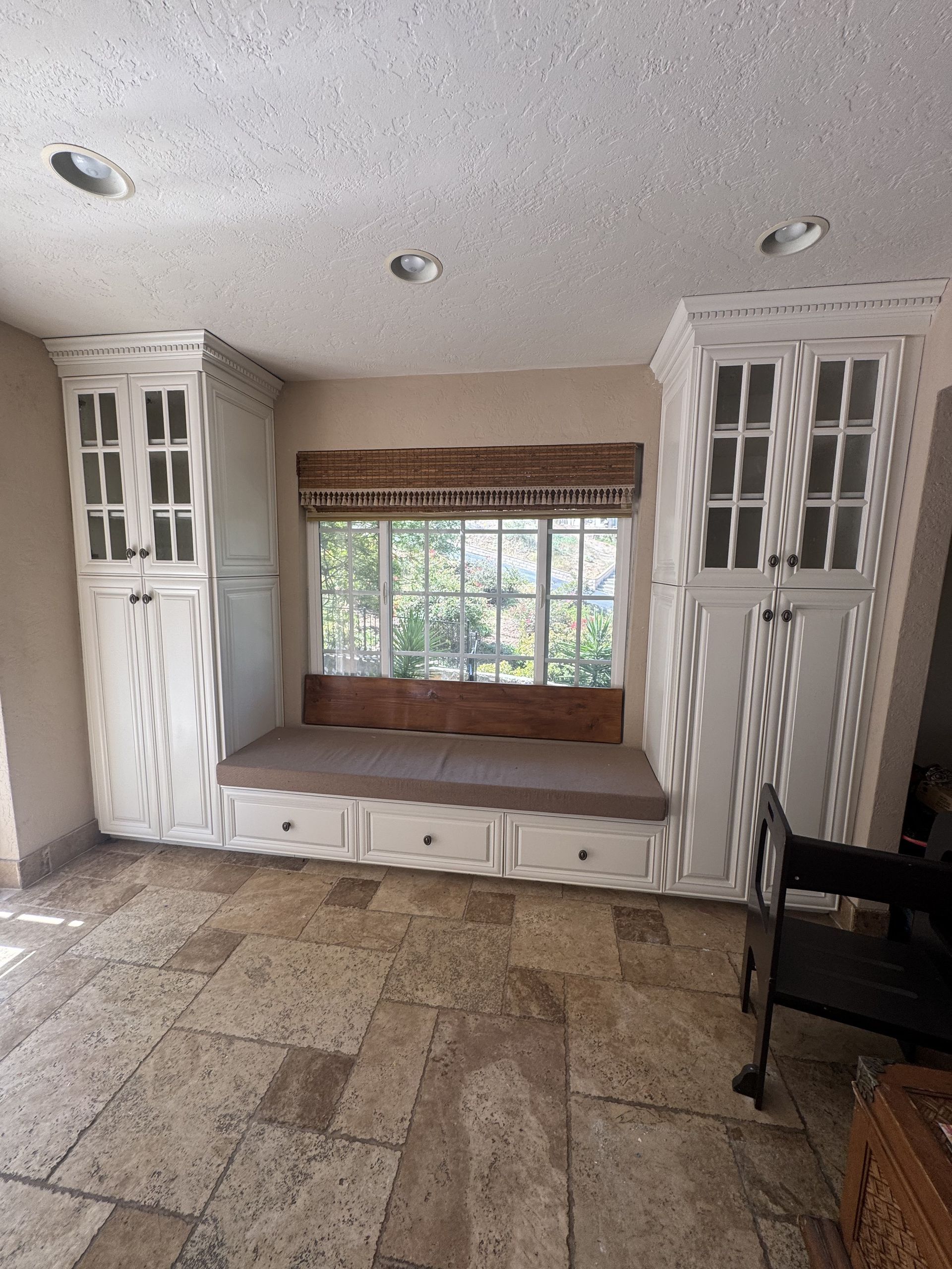 Empty room with built-in cabinets, large window seat, and stone tile floor.