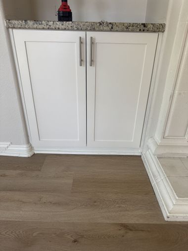 White built-in cabinet with silver handles in a hallway beside wood flooring and white trim.
