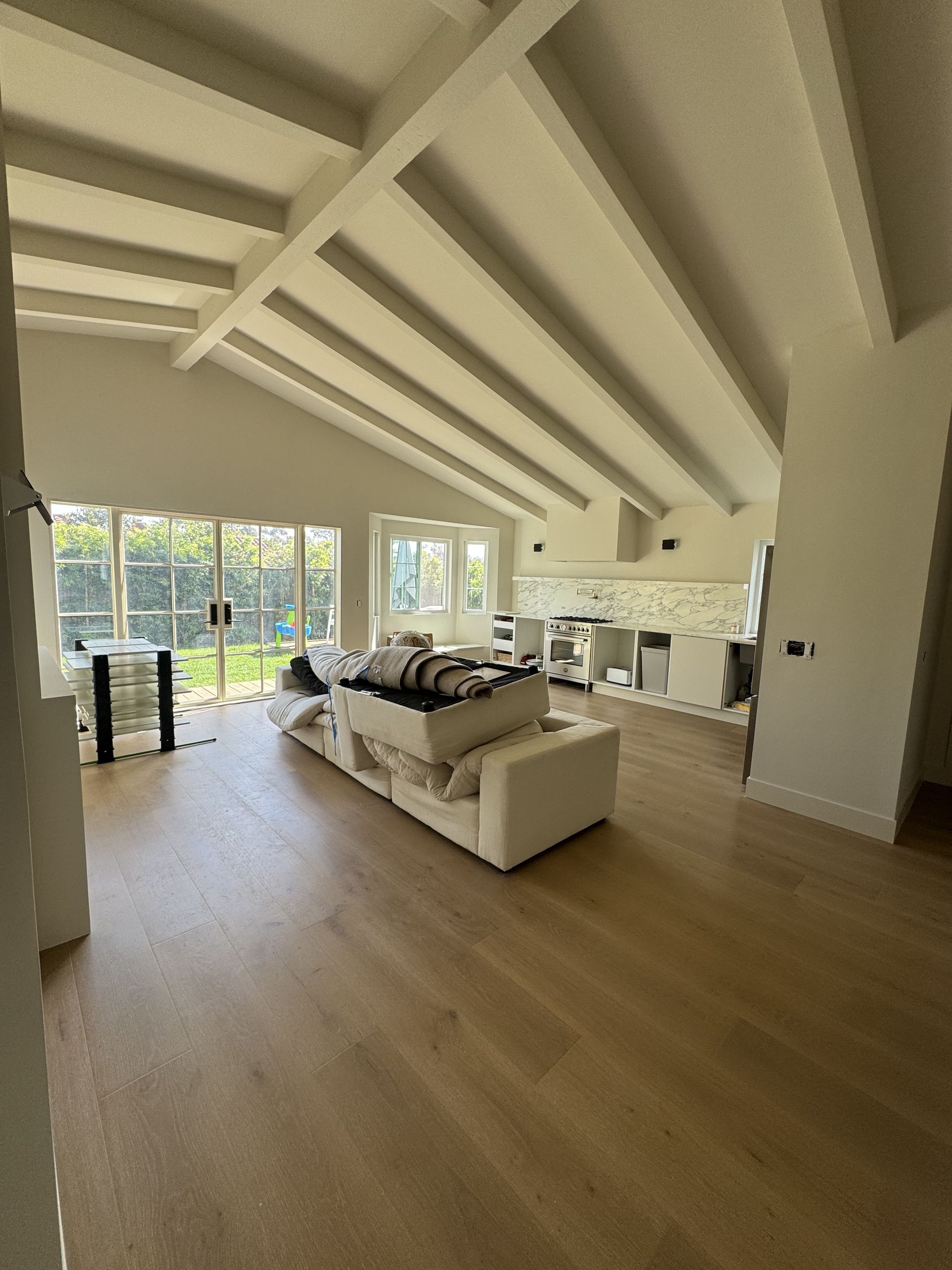 Bright open-plan living room with vaulted ceiling, white sofa, and glass doors overlooking a green yard