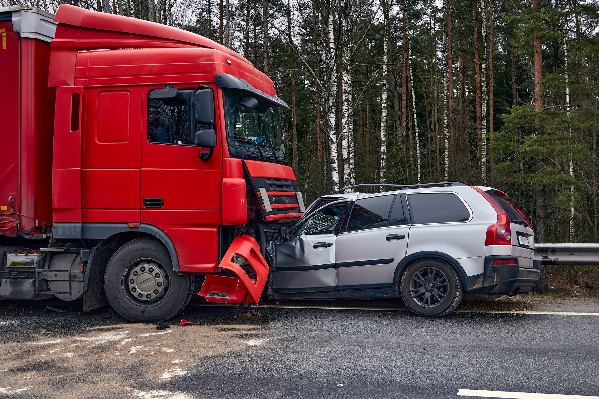 A red semi-truck collided into the rear of a silver SUV on a roadside near trees