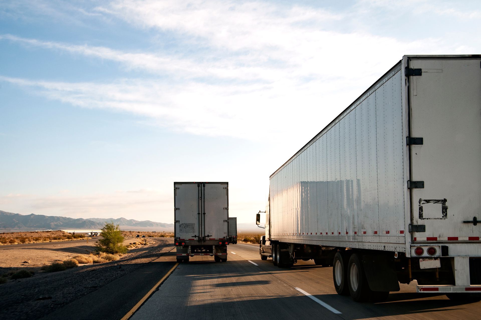 Two large semi-trucks driving on a highway through a desert landscape under a clear sky.