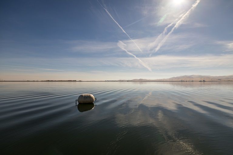 Small buoy floating on calm lake under bright sun, with rippled water and clear sky reflections