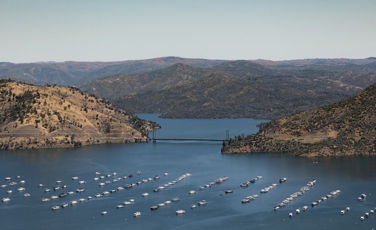 Scenic bay with many boats, surrounded by hills and a bridge in the distance.
