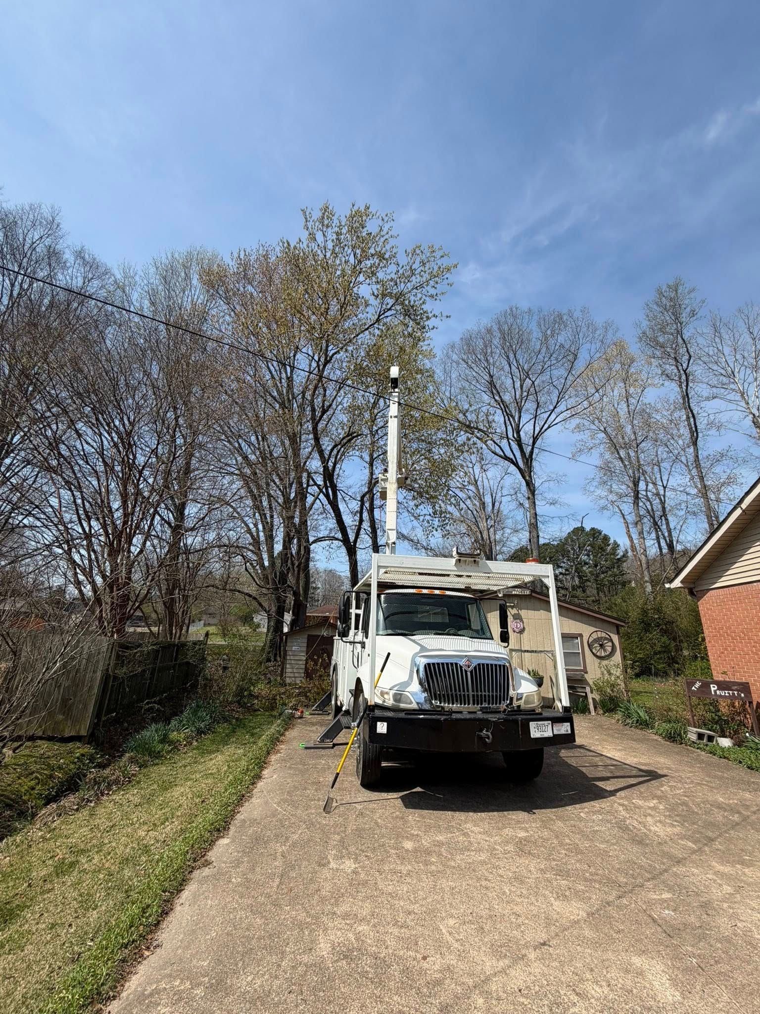 White utility truck with boom lift parked on a gravel driveway under a blue sky, trees behind it. White utility truck with boom lift parked on a gravel driveway under a blue sky, trees behind it.