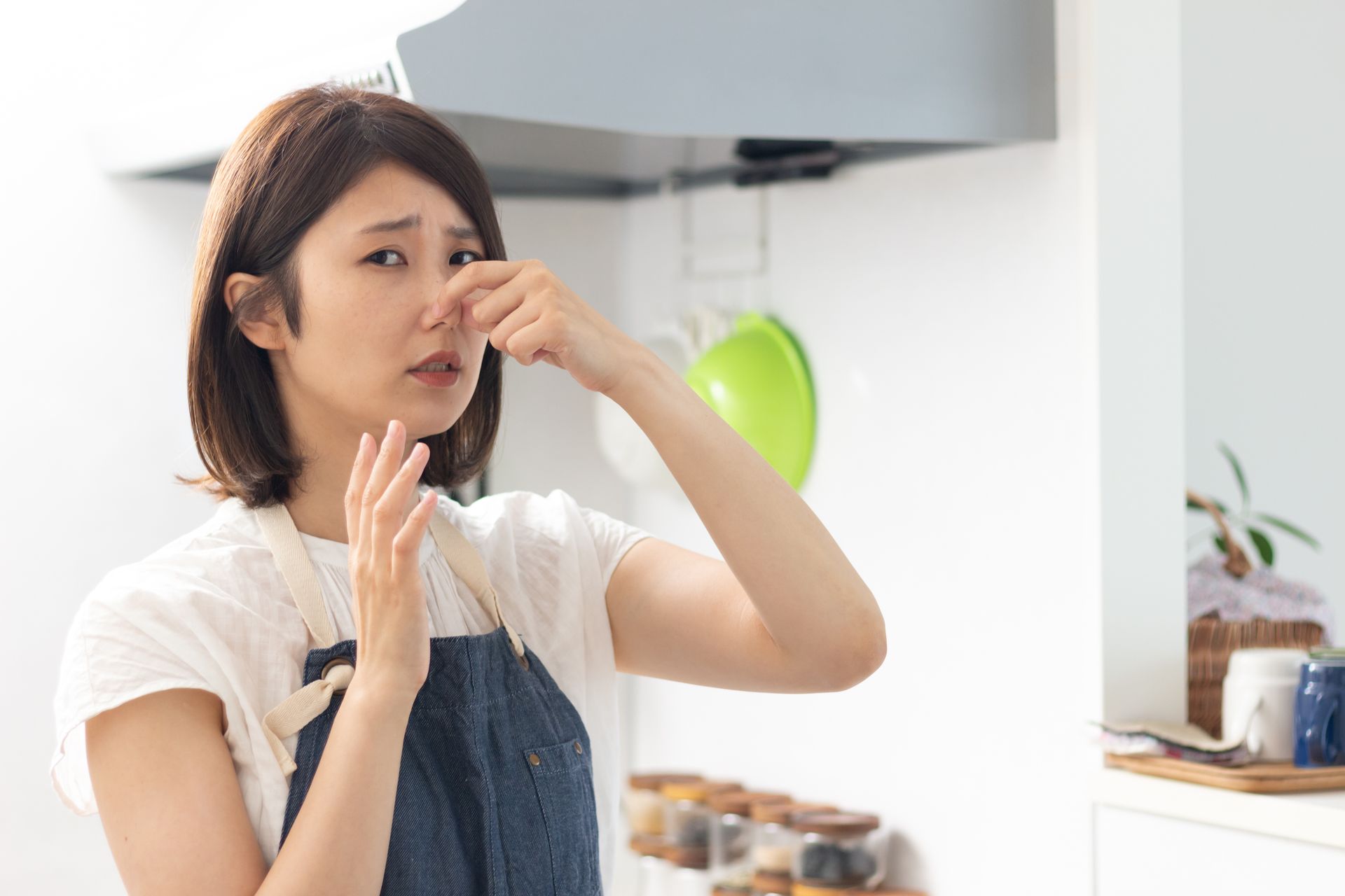 Woman covering her nose due to a bad smell in the kitchen