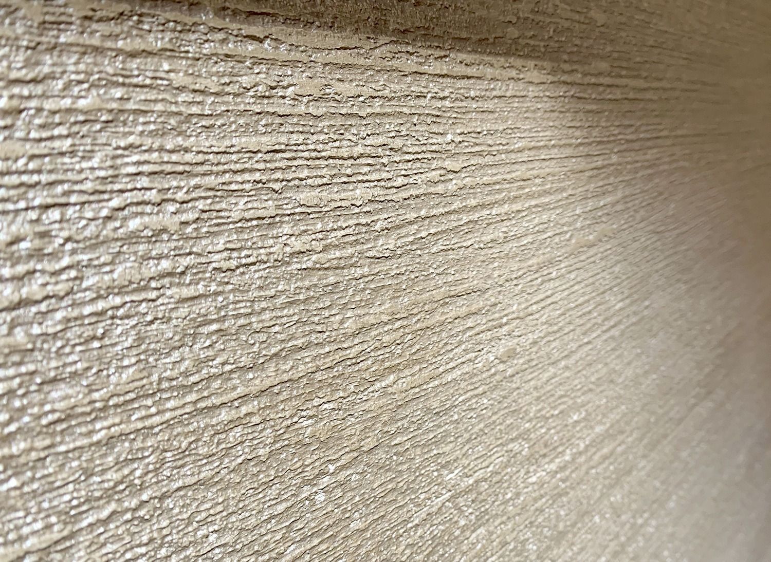 Primo piano di una parete beige con texture, scanalature orizzontali e illuminazione soffusa.