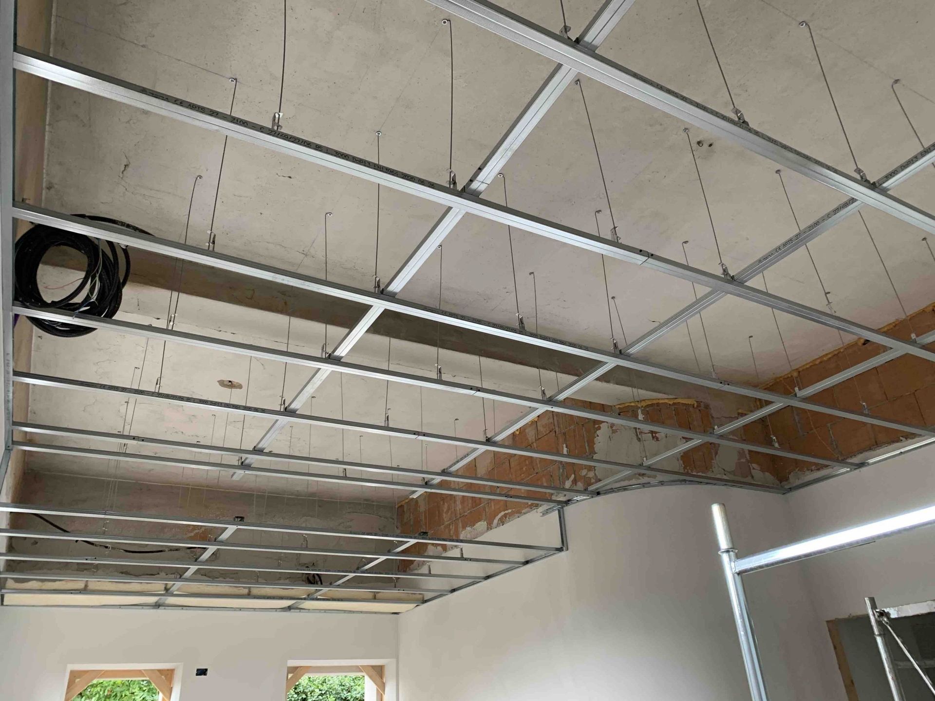 Struttura metallica a vista del soffitto e cavi penzolanti in una stanza in fase di ristrutturazione.