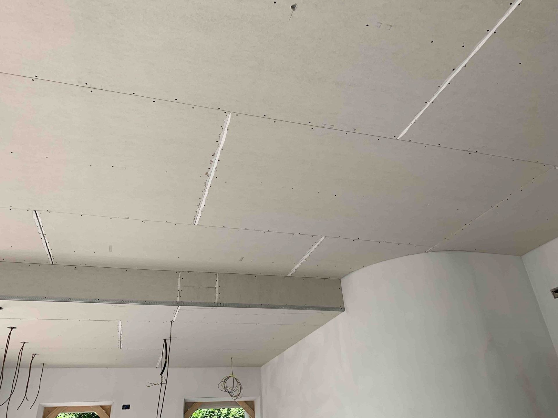 Soffitto non rifinito con giunture a vista e fili penzolanti in una stanza in costruzione.