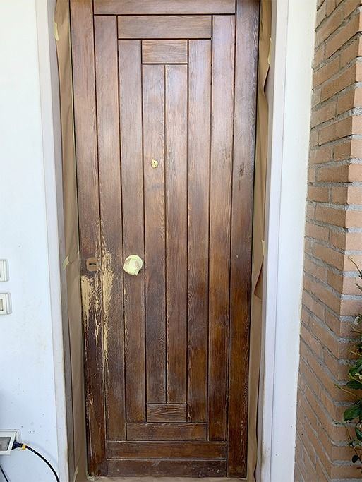 Porta d'ingresso in legno con maniglia in ottone incastonata in un ingresso in mattoni.