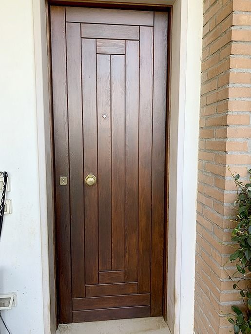 Porta d'ingresso in legno con spioncino e maniglia in ottone, inserita in un ingresso in mattoni e stucco.