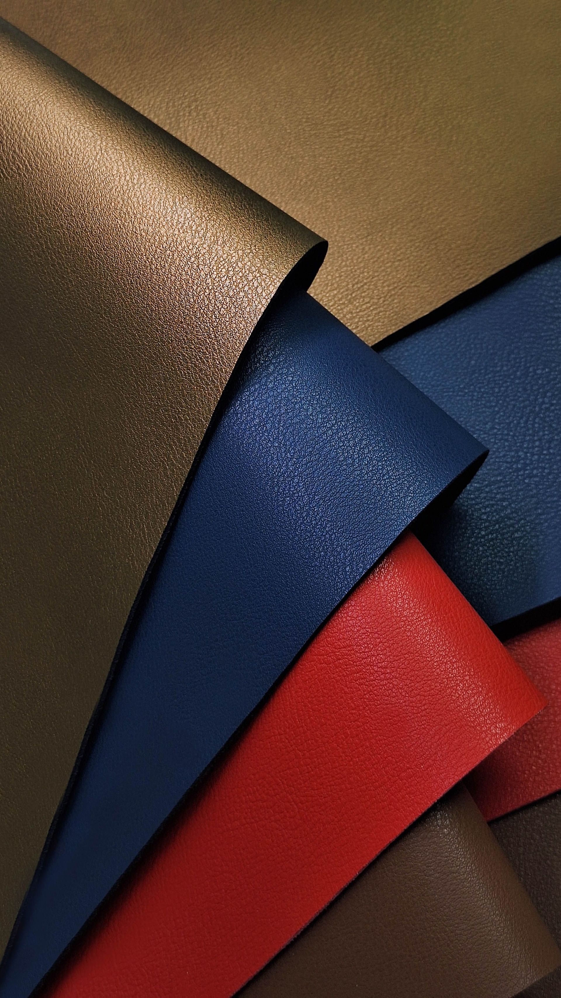Hojas de papel texturizado apiladas en tonos dorados, azul marino, rojos y marrones.