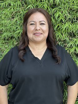 Smiling person in a black top standing before green foliage.
