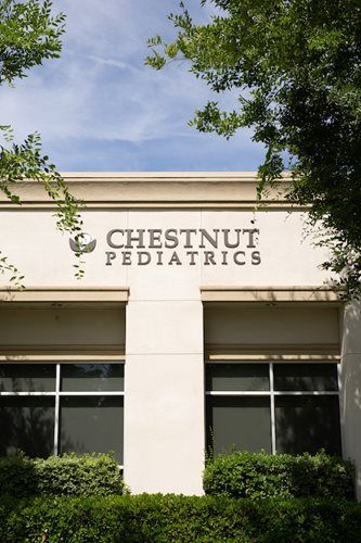 Chestnut Pediatrics sign on a beige building with windows and trees overhead
