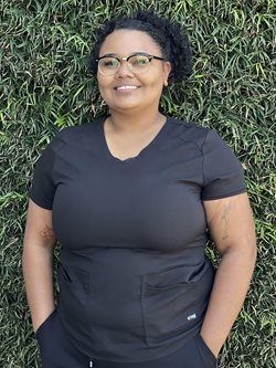Person in a black shirt smiling in front of a green leafy wall