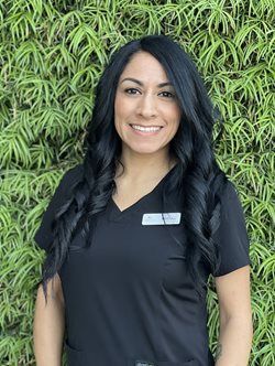 Smiling woman in black uniform standing before a green leafy wall