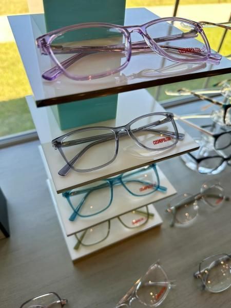 Display of eyeglass frames on white shelves in a store, including purple, gray, and turquoise styles