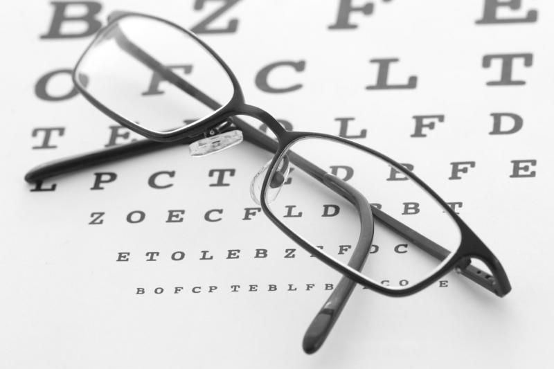 Black eyeglasses resting on an eye chart with scattered letters