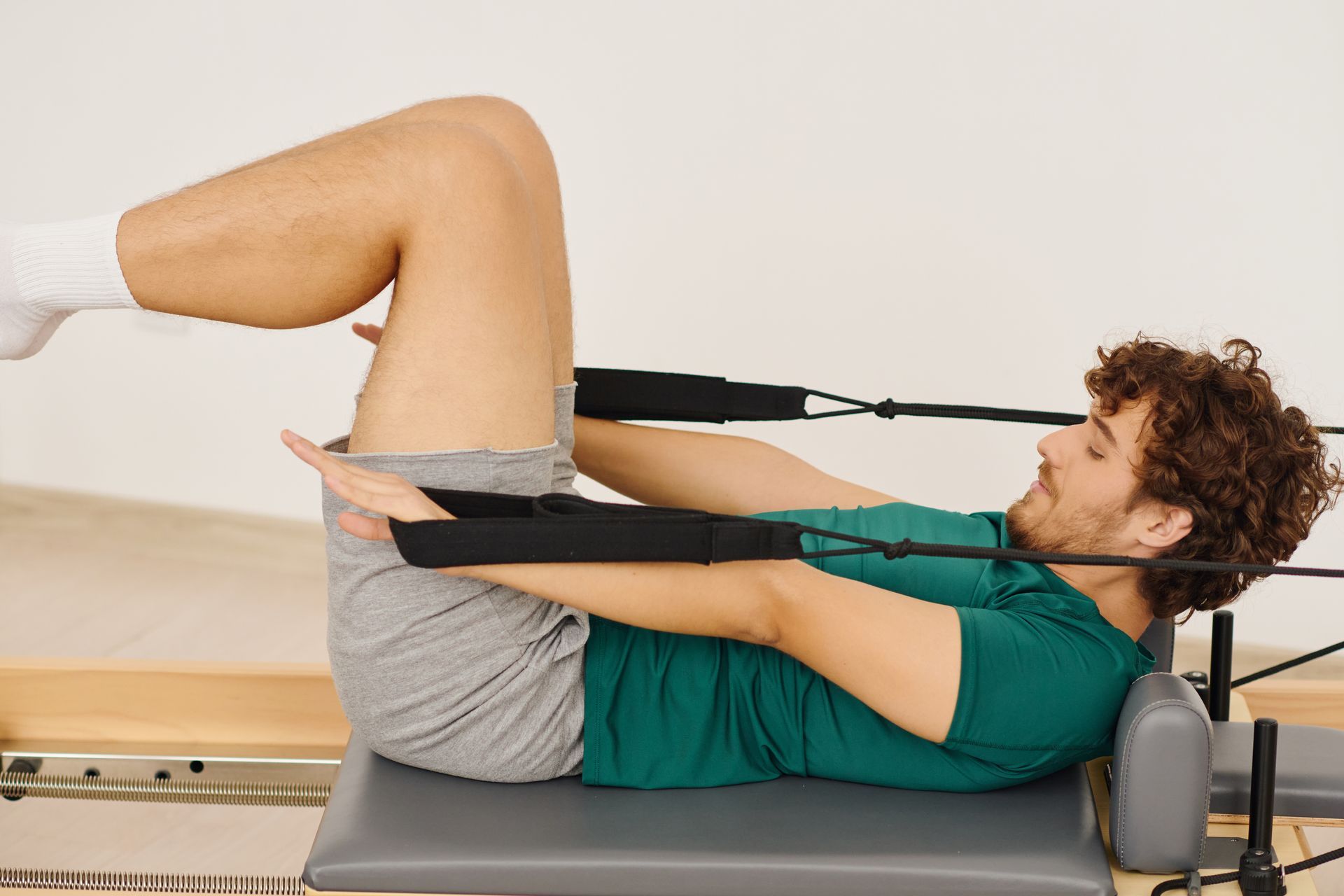 Person doing a Pilates exercise on a reformer, lying on back with knees bent and feet in straps